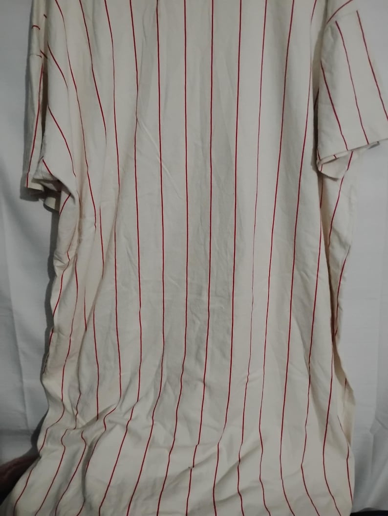 May include: Cream-colored, short-sleeved shirt with vertical red stripes. The fabric appears to be lightweight and slightly wrinkled. The shirt is a casual style, suitable for everyday wear.