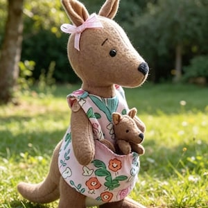 Könnte beinhalten: Ein braunes Filz-Känguru-Stofftier mit einer hellrosa Schleife am Ohr, das ein hellrosa Kleid mit buntem Blumenmuster trägt. Ein kleineres, passendes Känguru-Junges steckt in der Bauchtasche der größeren Känguru-Figur.