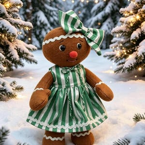 Pode incluir: Uma boneca de pão de mel castanha com cabeça redonda, nariz vermelho, olhos pretos e acabamentos brancos ondulados. A boneca usa um vestido às riscas verdes e brancas com um laço grande a condizer e acabamentos ondulados nas mangas.