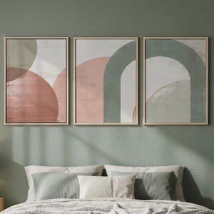 Peut inclure: Intérieur de chambre avec un lit aux draps clairs, des oreillers et une couverture grise. Au-dessus du lit, trois œuvres d'art abstraites encadrées aux tons neutres. Une table de chevet en bois avec une lampe est à gauche et une plante en pot à droite.