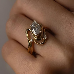 May include: A gold ring with a large, clear, marquise-cut diamond as the centerpiece. The ring features a unique, swirling design with smaller accent diamonds. The band is a polished gold, creating a luxurious look.