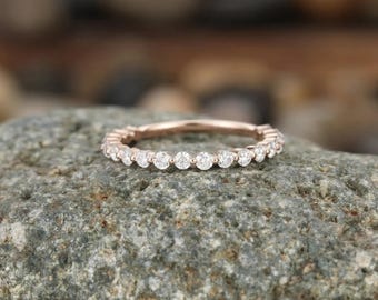 Op de afbeelding: Een roségouden ring met een doorlopende rij kleine, ronde, heldere en gefacetteerde stenen in een gedeelde zetting. Het metaal heeft een warme, roze metallic tint en de stenen zijn in een enkele, uniforme lijn rond de band gerangschikt.