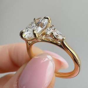 May include: A gold ring featuring a large marquise-cut centre stone flanked by two smaller pear-cut stones on each side. The band is crafted from polished yellow gold, and the setting holds five clear, faceted gemstones that reflect light.
