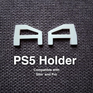 Może przedstawiać: Dwa białe wsporniki do uchwytu PS5. Tekst "PS5 Holder" jest wyświetlany poniżej wsporników, z napisem "Compatible with Slim and Pro" poniżej. Wsporniki znajdują się na ciemnoszarej, teksturowanej powierzchni.