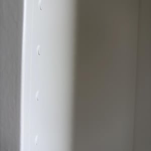 May include: A close-up of a white, smooth surface with four curved indentations. The surface is divided by a vertical line, with the right side in shadow. The indentations are evenly spaced.