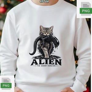 Può includere: Una felpa bianca a maniche lunghe con la grafica di un gatto tigrato che porta in bocca una creatura aliena nera. Sotto l'illustrazione, il testo recita ALIEN THE SHORT VERSION con una piccola icona a forma di testa di alieno.