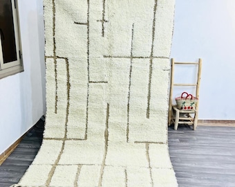 May include: A large, rectangular off-white rug with a geometric design in brown. The rug has a shaggy texture and is adorned with tassels along the edges. The design features vertical and horizontal lines, creating a modern, minimalist aesthetic.