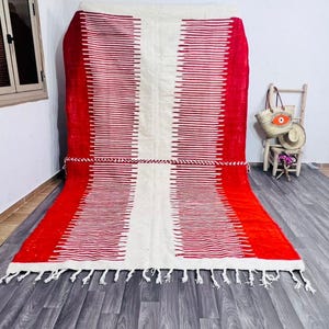 May include: A rectangular rug with a red and white striped pattern. The rug has a white central section and red borders. A decorative rope is tied around the middle. The rug has white fringe along the bottom edge.
