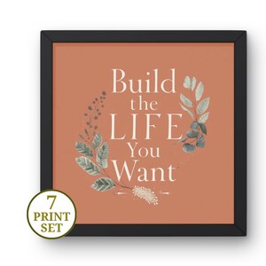 May include: Framed art print with the text "Build the LIFE You Want" in white, surrounded by a botanical design. The print has a terracotta background and is set in a black frame. A circular sticker in the lower left corner reads "7 PRINT SET".