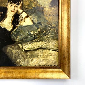 May include: A framed oil painting of a woman in a black hat and dress, resting her head on her hand. The painting has a gold frame and is in a classic style, with a muted color palette of gold, black, and green.