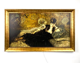 May include: A framed print of a woman reclining on a chaise lounge, dressed in a black gown. The artwork has a gold frame and a warm color palette with gold, black, and green tones. The woman is the focal point of the image.