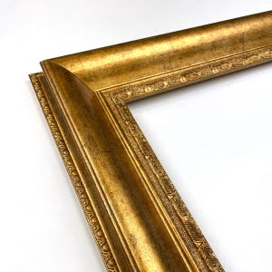 May include: Close-up of a gold picture frame corner. The frame has an ornate design with a textured surface. The frame is made of wood and has a metallic gold finish. The frame is angled, showing the corner joint.