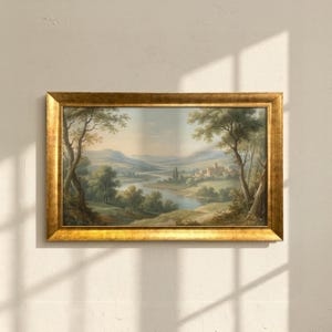 Op de afbeelding: Een ingelijst landschapsschilderij met een goudkleurige, sierlijke lijst. Het kunstwerk toont een serene vallei met een rivier, bomen en een ver dorp. Het kleurenpalet omvat groen, blauw en aardetinten, wat een rustige sfeer creëert.