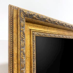 May include: Ornate gold picture frame with a black interior. The frame features detailed carvings and a distressed finish, adding a vintage aesthetic. The frame's design includes a beaded edge and decorative corner accents.