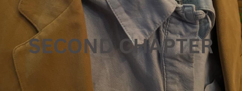 May include: Close-up of a tan suede blazer and a light blue button-down shirt. The text "SECOND CHAPTER" is visible across the image. The blazer has a classic notched lapel.