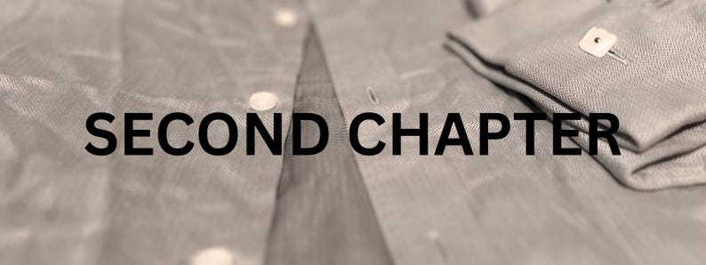 May include: Close-up of a light gray button-down shirt with the text "SECOND CHAPTER" in black. The shirt is partially unbuttoned, with the cuff of the sleeve folded over, showing a button.