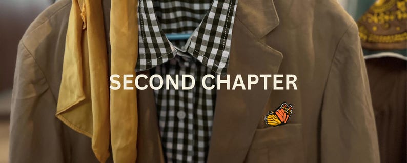 May include: A tan blazer with a black and white checkered shirt underneath, a yellow scarf, and a butterfly pin. The text "SECOND CHAPTER" is displayed across the image. The blazer is hanging on a hanger.