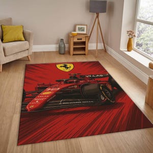 May include: A red and black area rug featuring a Formula 1 race car design. The rug has a red background with a graphic of a race car and the Ferrari logo. The rug is rectangular and placed on a hardwood floor.