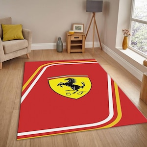 May include: A red rectangular rug featuring the Ferrari logo. The logo is a black prancing horse on a yellow shield with the letters "SF". The rug has white and yellow stripes along the edges.