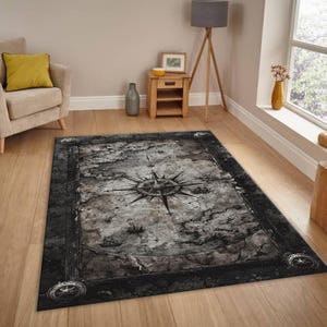 May include: A rectangular area rug featuring a detailed compass rose design in shades of gray and black. The rug has a distressed, vintage map aesthetic with illustrations of ships and clouds. The border is dark with decorative elements.