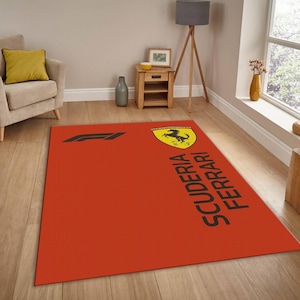 May include: A rectangular area rug featuring a vibrant red background with the black Formula 1 logo on the left side and the yellow Scuderia Ferrari shield emblem on the right, accompanied by the black text Scuderia Ferrari printed vertically.