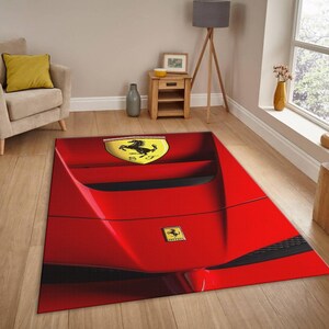May include: A red rectangular area rug featuring a design inspired by a Ferrari car. The rug has a glossy finish and includes the Ferrari logo in yellow and black. The rug is placed on a hardwood floor in a living room setting.