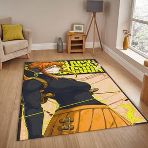 Puede incluir: Una alfombra rectangular con un personaje de la serie de anime Black Lagoon. La alfombra muestra un personaje femenino con una parte superior negra y una falda naranja, con el título del programa en amarillo. La alfombra está colocada sobre un suelo de madera.