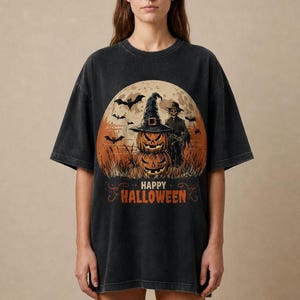 Puede incluir: Una camiseta negra con efecto lavado al ácido que presenta un estampado gráfico de dos calabazas apiladas con un sombrero de bruja, un espantapájaros, murciélagos y una luna llena. El texto "HAPPY HALLOWEEN" aparece en naranja al frente.