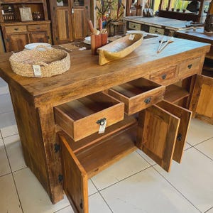 May include: A large, rustic wooden kitchen island with multiple drawers and cabinet doors. The island is made of light brown wood and has a natural finish. A woven basket and wooden bowl sit on top. The drawers and doors are open, revealing interior storage.