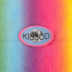 May include: An oval sticker with the word "KISSCO" in silver letters, a disco ball graphic, and a pink border. The background is a gradient of rainbow colors, including blue, green, pink, and yellow.
