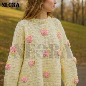 Op de afbeelding: Een crèmekleurige trui versierd met meerdere roze rozen applicaties. De trui heeft een ronde hals en lange mouwen. De rozen hebben gele en groene accenten. De merknaam "NEORA APPAREL" is linksboven zichtbaar.