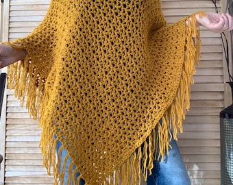 Peut inclure: Un poncho en crochet jaune moutarde avec un motif en losanges ajouré et une encolure en V. Le vêtement présente un ourlet pointu fini par de longues franges pendantes le long des bords, créant un aspect texturé et superposé.