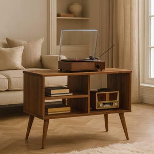 Puede incluir: Consola de tocadiscos de madera de estilo moderno de mediados de siglo, con tocadiscos, radio y estantes de almacenamiento. La consola marrón tiene una cubierta de plástico transparente. La habitación tiene una paleta de colores neutros.