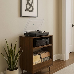 May include: A mid-century modern style record player and stereo system on a dark wood cabinet. The cabinet has a shelf for the stereo receiver and a lower shelf for vinyl records. A framed abstract art piece hangs above the cabinet.