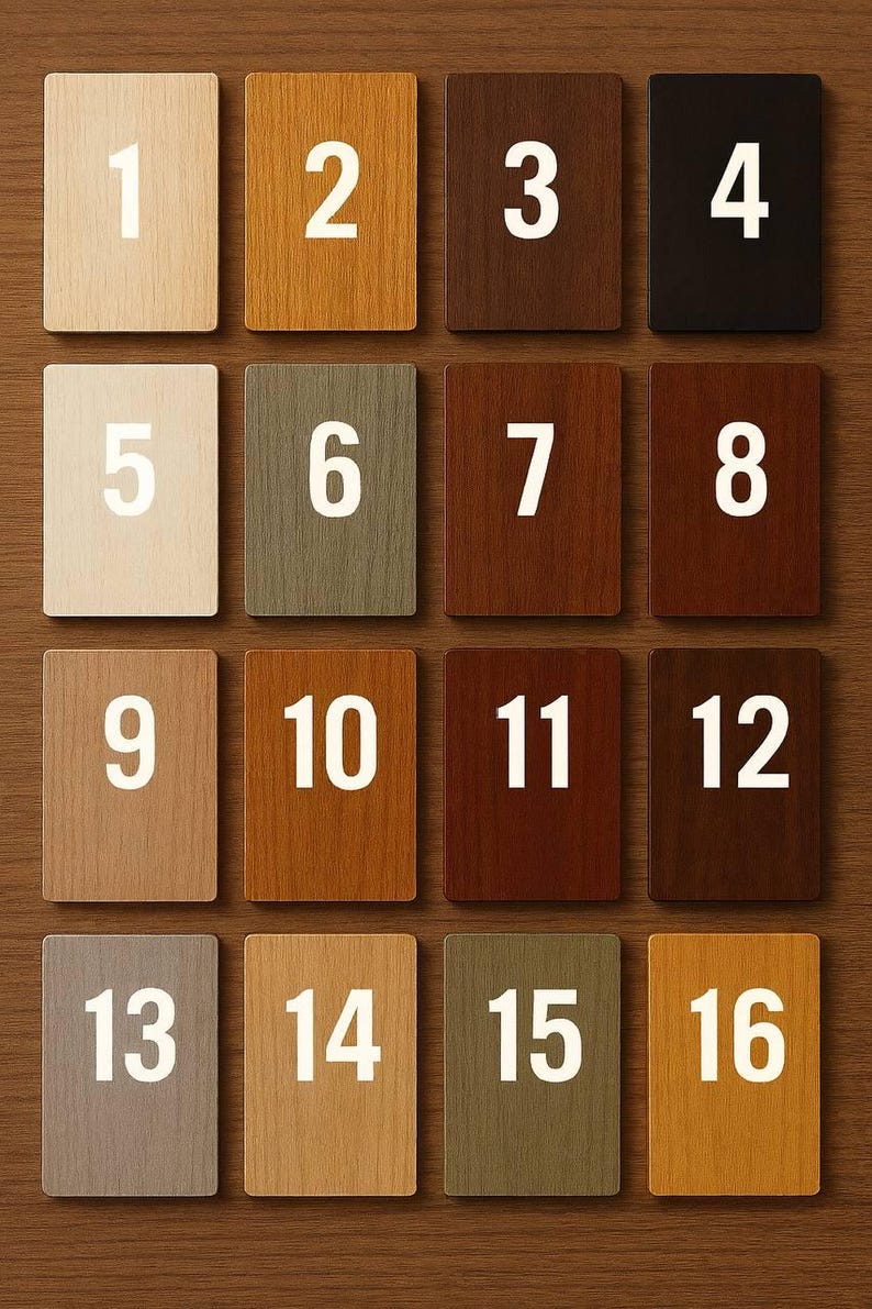May include: Sixteen wooden square tiles with different wood stain colors, numbered 1 through 16 in white. The tiles are arranged in a grid pattern on a wooden surface, showcasing a variety of hues from light beige to dark brown.