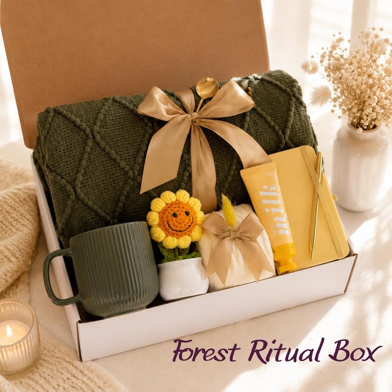 May include: A gift box containing a dark green knit blanket tied with a gold ribbon, a ribbed dark green mug, a small crocheted sunflower in a white pot, a yellow notebook with a gold pen, and a tube of milk lotion with a gold bow.