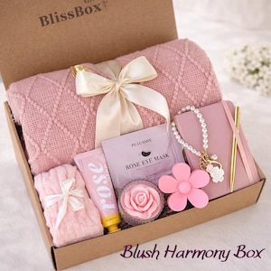 May include: A gift box from "BlissBox" containing pink items. It features a blanket, notebook, bracelet, flower-shaped item, rose soap, rose lotion, and a "Rose Eye Mask" packet. The box is labelled "Blush Harmony Box".