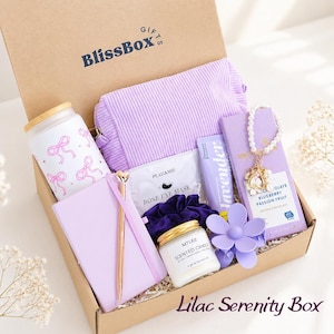 May include: A gift box labeled BlissBox containing a frosted glass tumbler with pink bows, a ribbed lavender pouch, a rose eye mask, a lavender tube, a chocolate bar, a pearl bracelet, a gold pen, a lavender notebook, a candle, and a flower clip.