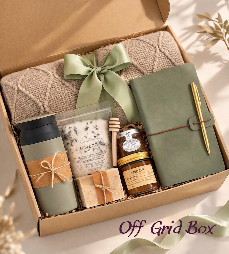 May include: A gift box containing a beige cable-knit blanket with a sage green ribbon, a sage green tumbler with a brown band, a pouch of lavender bath soak, a wooden honey dipper, a bar of soap, a jar of honey, a candle, and a sage green journal with a gold pen.