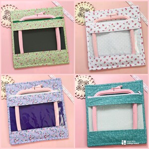 May include: Four square fabric pouches with floral or solid patterns, each featuring a clear plastic window and a pink plastic embroidery hoop frame. The pouches include a zippered compartment at the top and a quilted texture throughout the fabric.