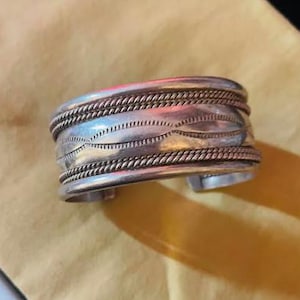May include: A silver cuff bracelet with a braided design and a wavy pattern.