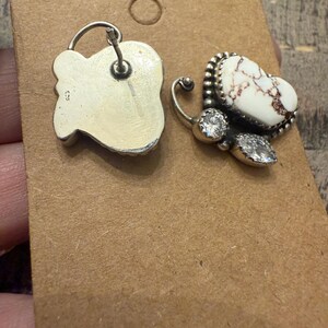 May include: A pair of silver-toned butterfly earrings. One earring features a white stone with brown veining, surrounded by a beaded border and two clear, round stones. The other earring is a silver-toned, irregular shape.