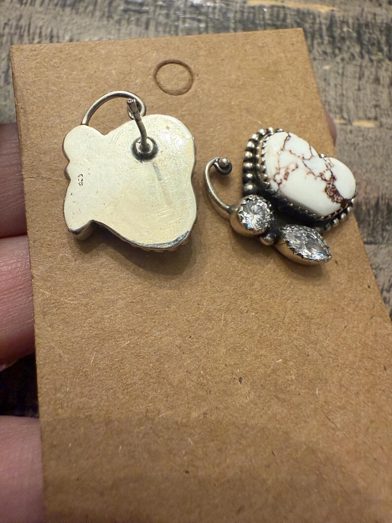 May include: A pair of silver-toned butterfly earrings. One earring features a white stone with brown veining, surrounded by a beaded border and two clear, round stones. The other earring is a silver-toned, irregular shape.
