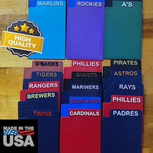 May include: A collection of colorful file folder organizers, each labeled with a different Major League Baseball team name. The folders are in various colors, including red, blue, green, and purple. A "High Quality" sticker and a "Made in the USA" sticker are also visible.