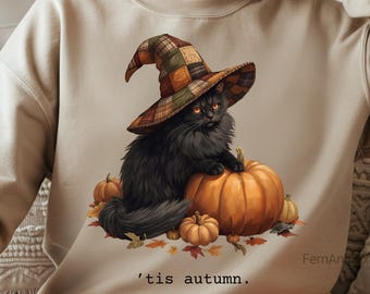 May include: Beige sweatshirt featuring a black cat wearing a plaid witch hat, sitting on a large orange pumpkin. Smaller pumpkins and autumn leaves surround the cat. The text "'tis autumn" is printed below the image.