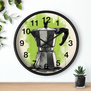 Op de afbeelding: Een ronde wandklok met een zwart frame, met een koffiezetapparaat ontwerp. De wijzerplaat heeft een groene achtergrond met zwarte cijfers en wijzers. De klok staat op een houten oppervlak. De diameter van de klok is ongeveer 30 cm.