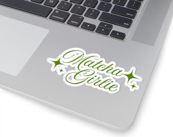Könnte beinhalten: Ein weißer Aufkleber mit den Worten "Matcha Girlie" in grüner, kursiver Schrift. Der Aufkleber hat grüne Sternchen-Akzente auf beiden Seiten des Textes. Der Aufkleber befindet sich auf einem silbernen Laptop.