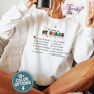 Peut inclure: Sweat-shirt blanc avec l'inscription "12 Days of CT Scans" en lettres colorées. Le motif comprend une liste de scénarios humoristiques liés aux tomodensitogrammes. Le sweat-shirt comporte également un graphique "10+ Color Options".