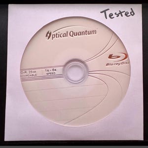 May include: A white Optical Quantum Blu-ray Disc with the text "Blu-ray Disc" and "Tested" written on the packaging. The disc has the text "D-R 25GB RECORDABLE" and "1x - 6x SPEED".