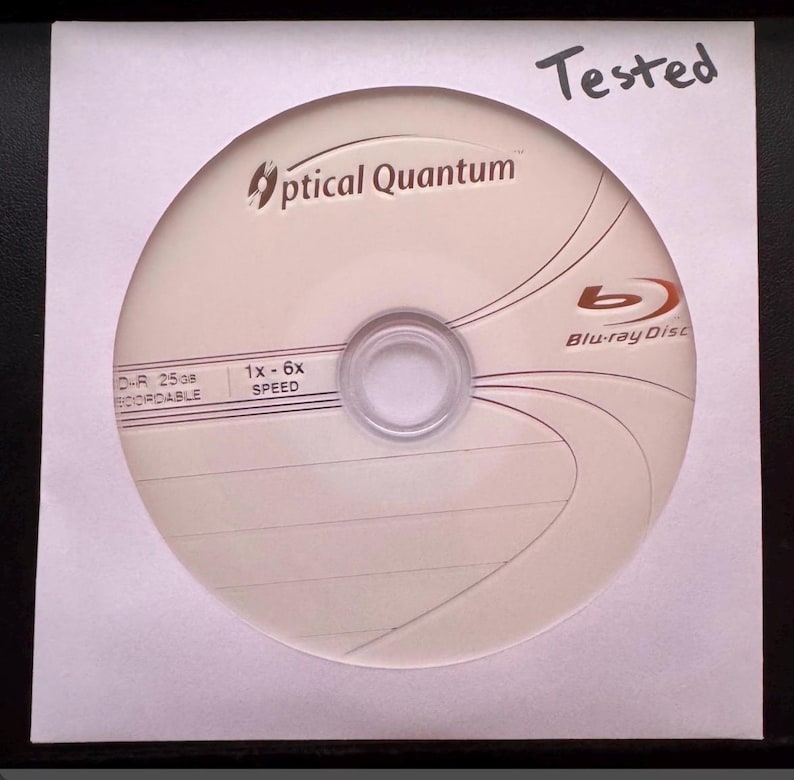 May include: A white Optical Quantum Blu-ray Disc with the text "Blu-ray Disc" and "Tested" written on the packaging. The disc has the text "D-R 25GB RECORDABLE" and "1x - 6x SPEED".